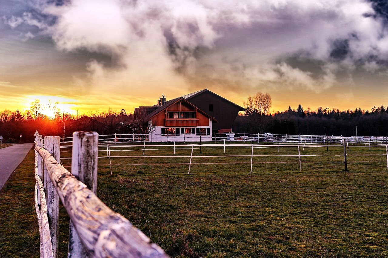 A picturesque farmhouse at sunset with fields and a dramatic sky in the rural countryside.