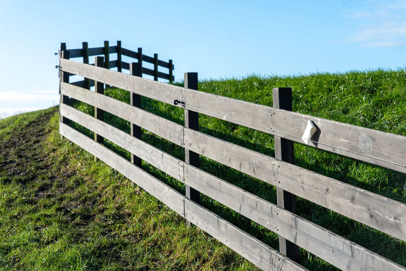 A long wooden fence along a grassy hill under a clear blue sky captured in daylight.