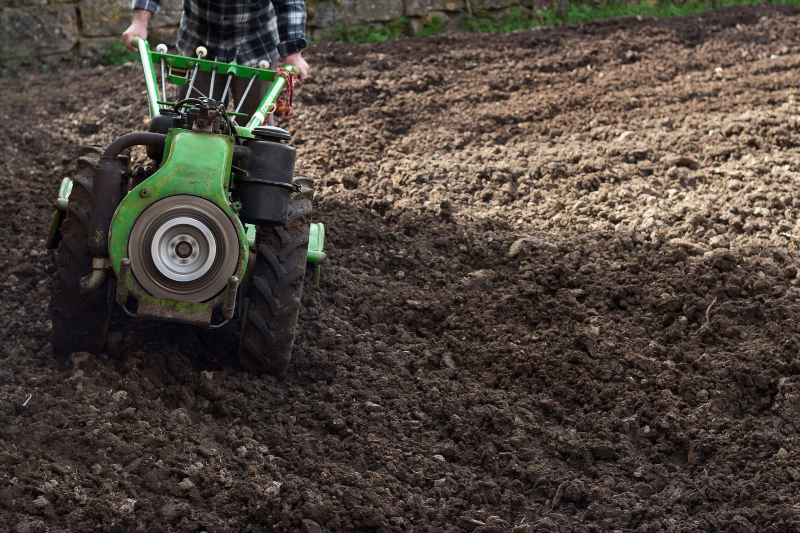 A farmer using a small green tractor to cultivate soil in a rural field.